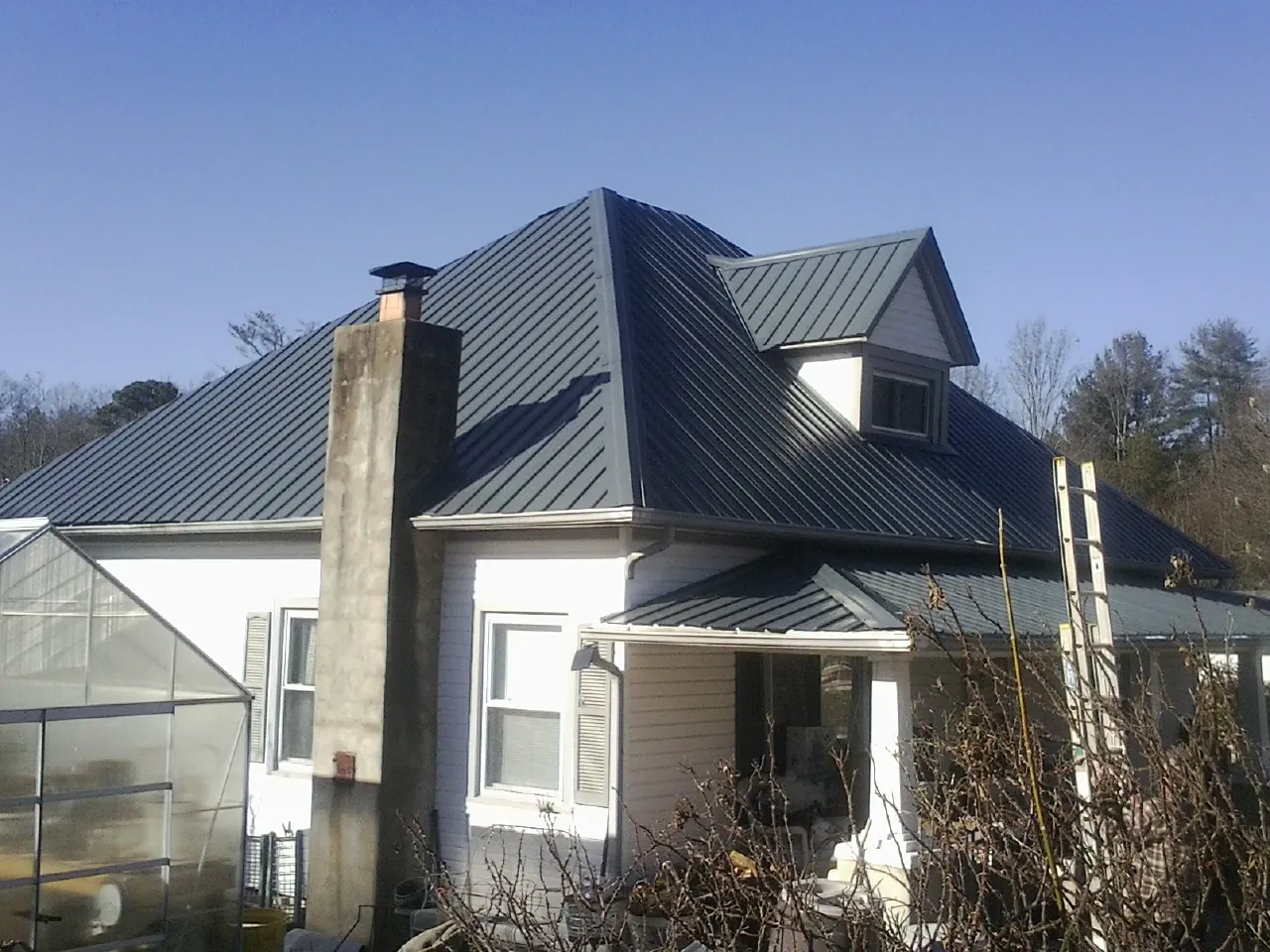 Dark blue standing seam metal roof on a white farmhouse with dormer — Slate & Tile Roof Repair by Roofing Brothers in Ferris