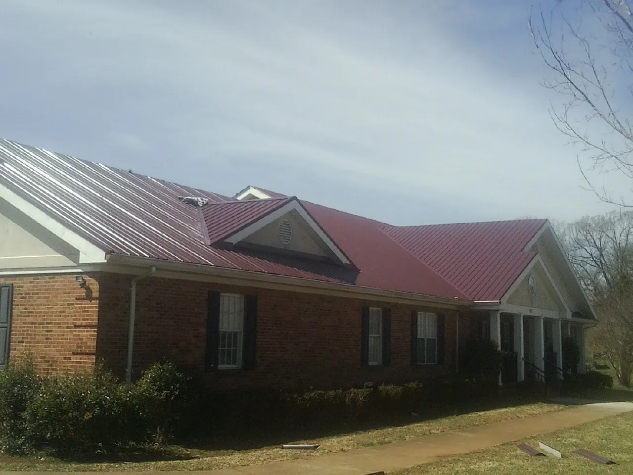 Red metal roof with gabled entries on a long brick building, from a Hail Damage Roof Repair job in Ferris