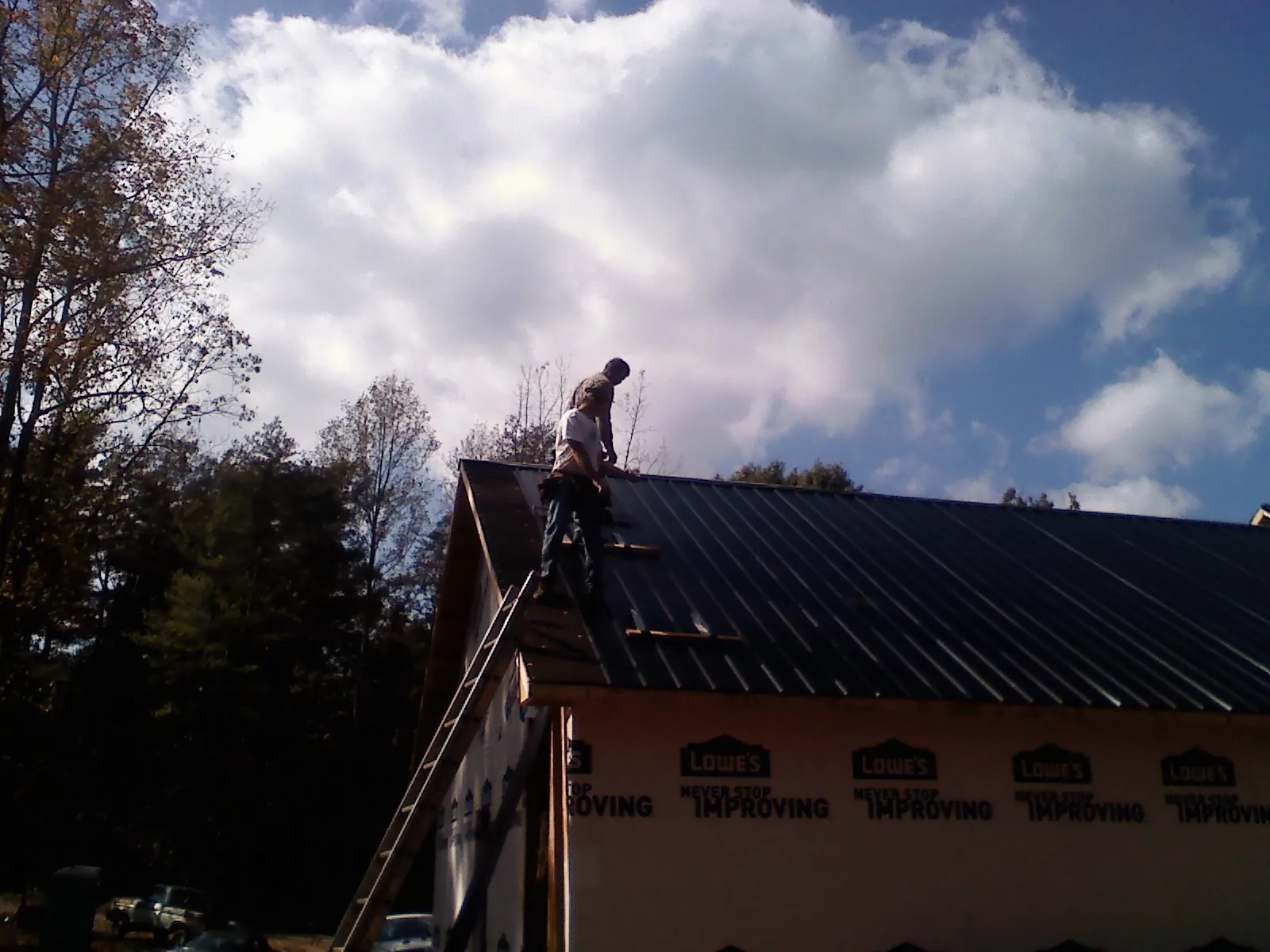 Roofer fastening dark metal panels high against a cloudy sky, from a Roof Inspection job in Ferris